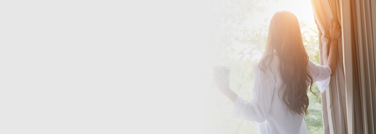 Woman looking outside while holding the curtains.